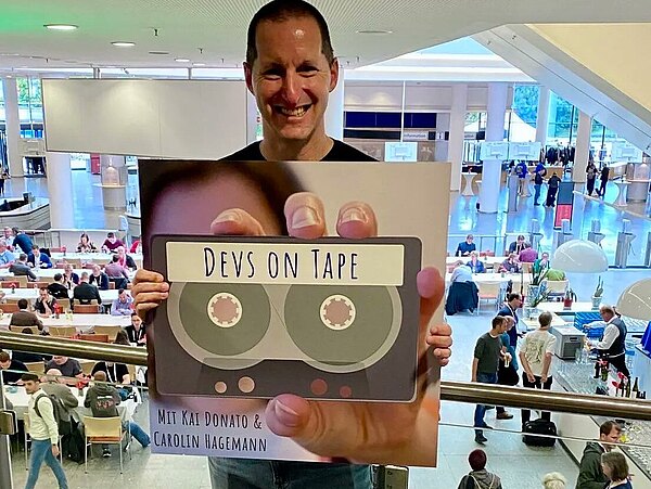 Connor McDonald auf der K+A mit dem Keyvisual des Podcast.